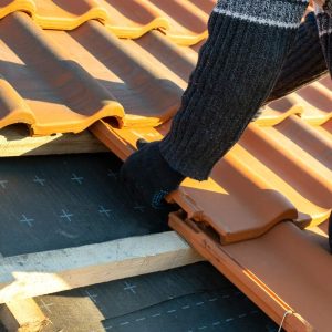 primer-plano-manos-trabajador-instalando-tejas-ceramica-amarillas-montadas-sobre-tablas-madera-que-cubren-techo-edificio-residencial-construccion